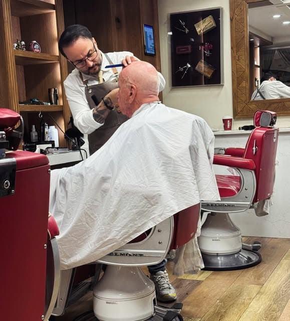A barber working on a client in the red chair